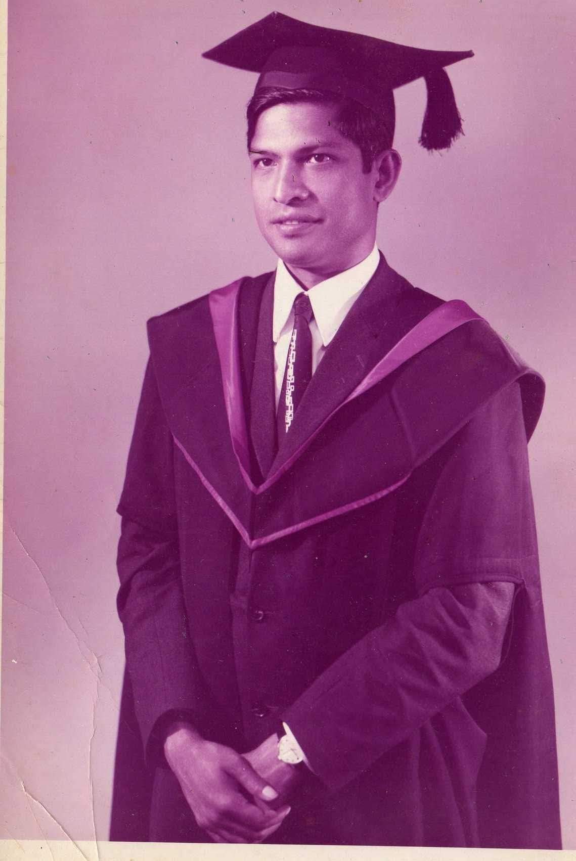 A young man in graduation robes and cap, standing formally and looking slightly to the side.